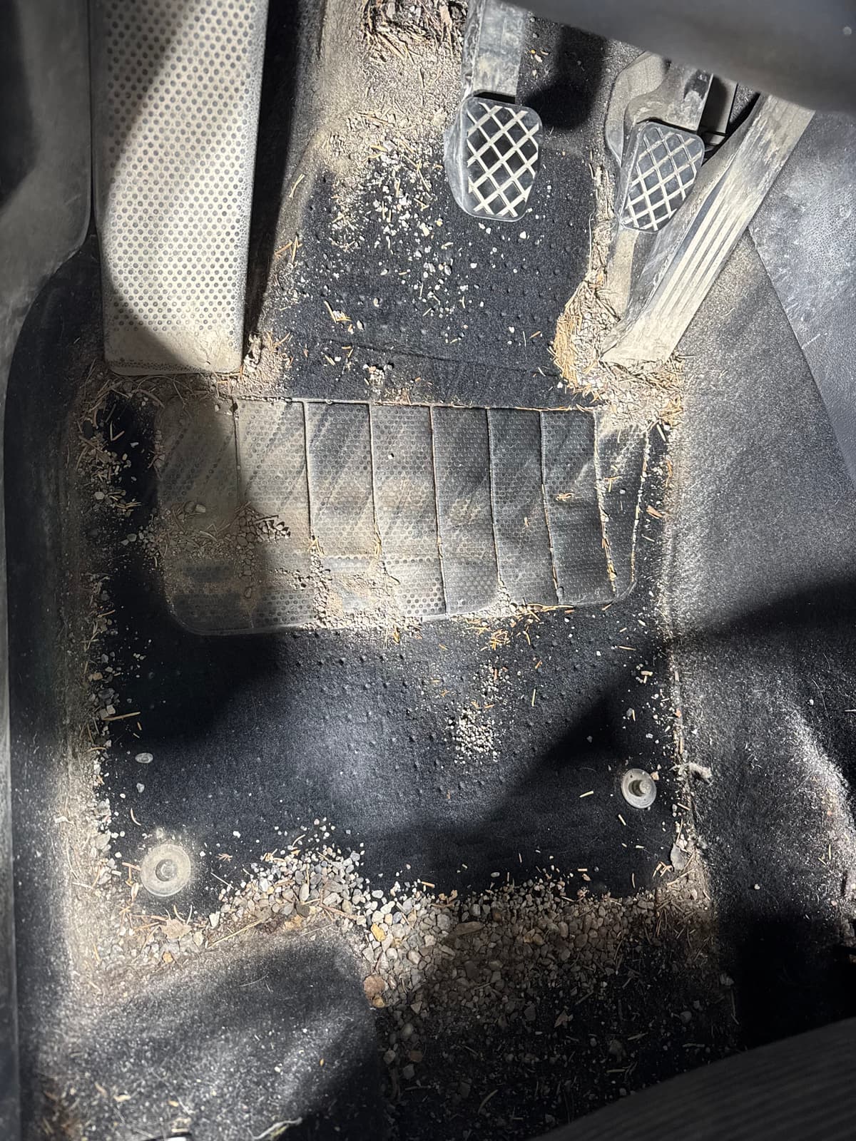 Heavily soiled driver's footwell with dirt and debris covering carpet and floor mat before professional interior detail