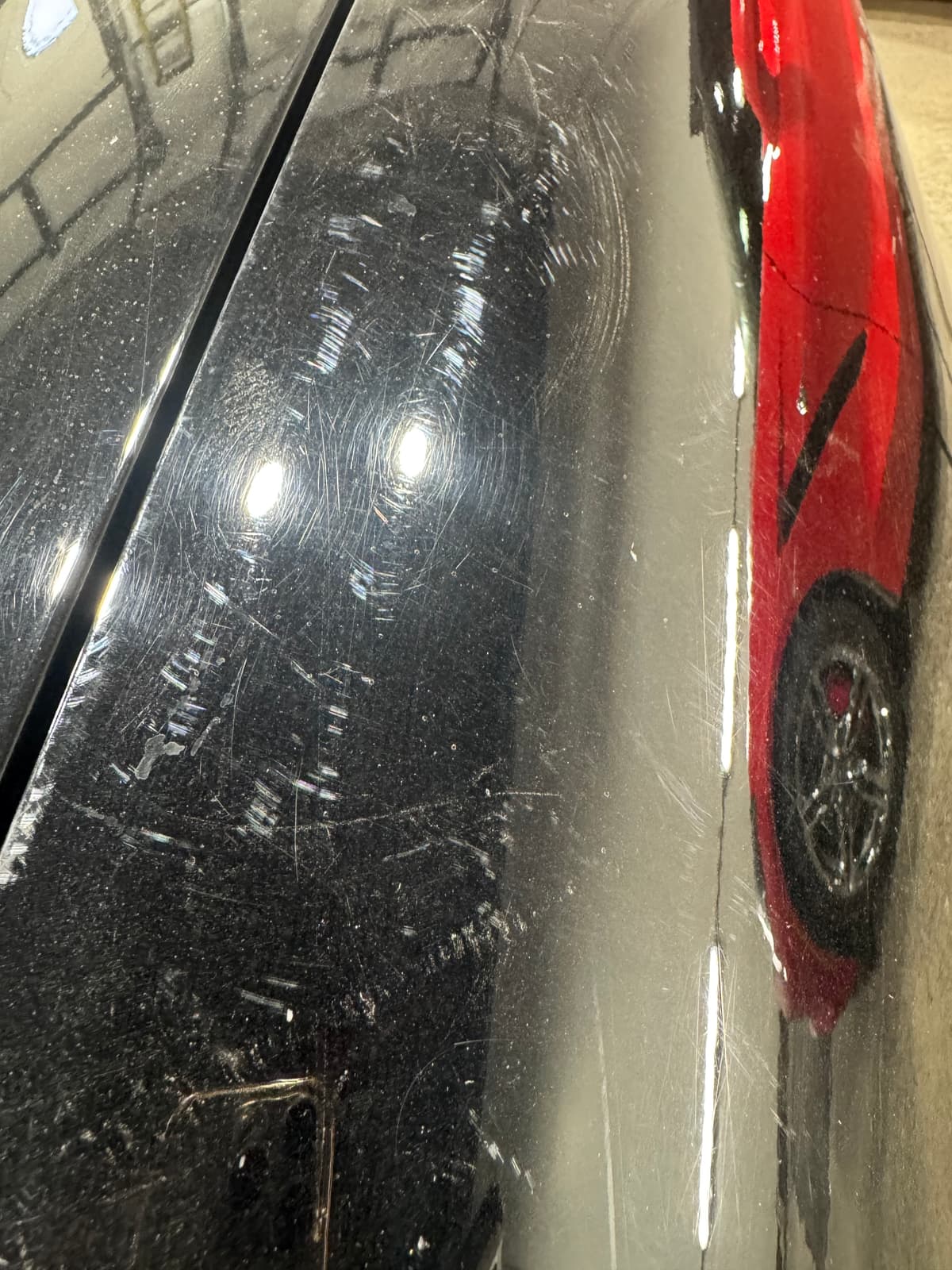 Black vehicle paint showing heavy swirl marks, scratches and oxidation before professional paint correction